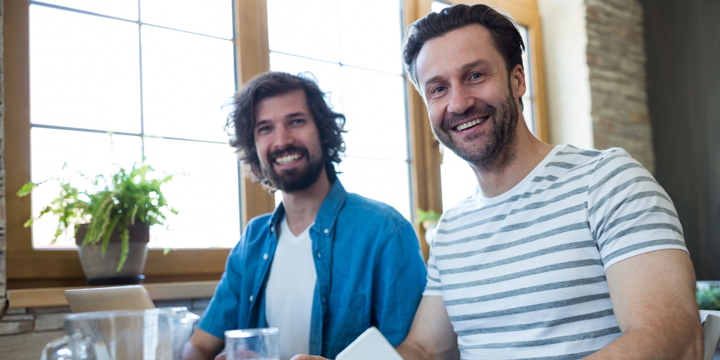 Two happy men smiling while sitting at a table | Source: Magnific
