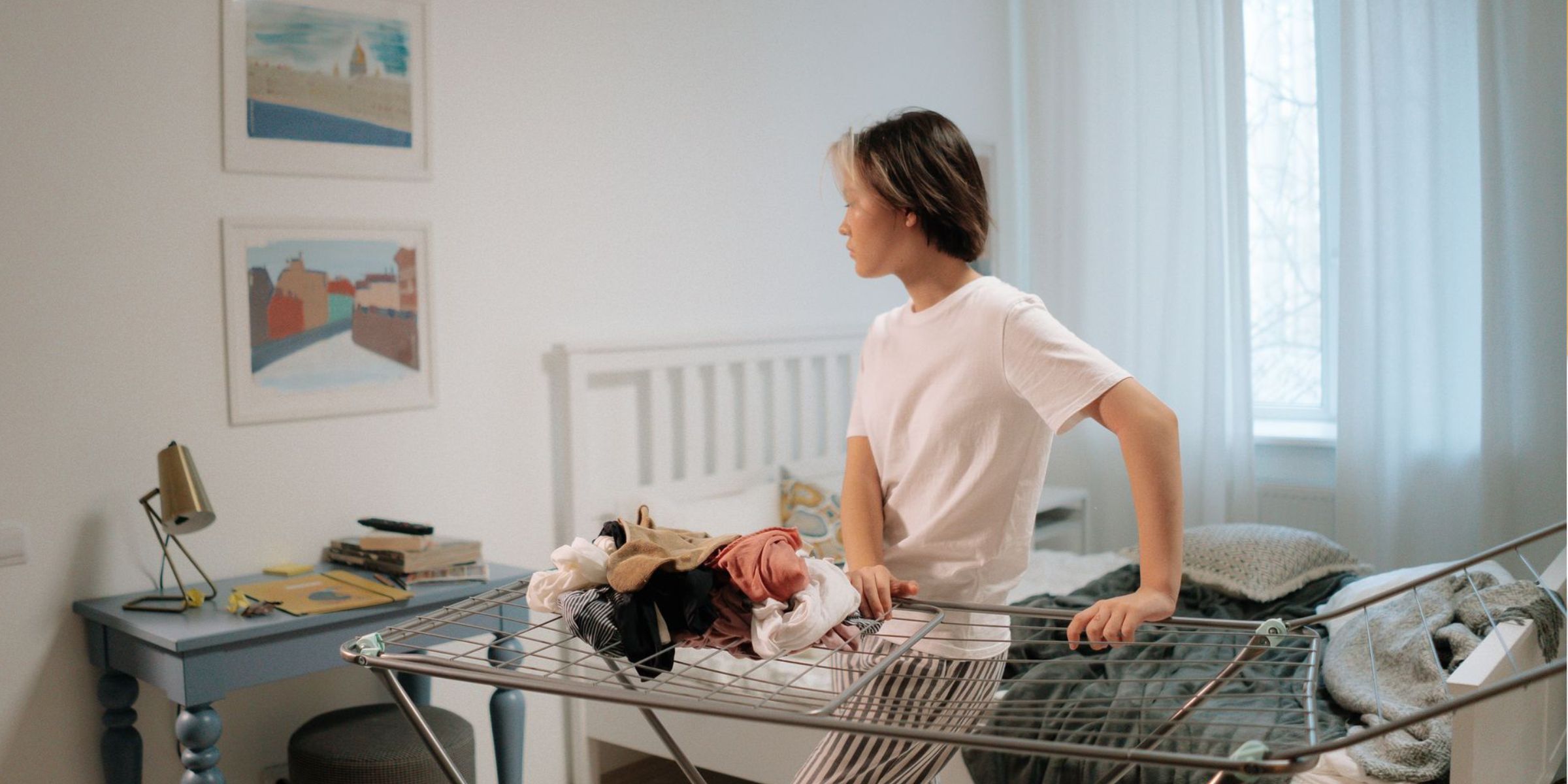 A young woman stands in a stylish bedroom, organizing clothes on a drying rack | Source: Pexels