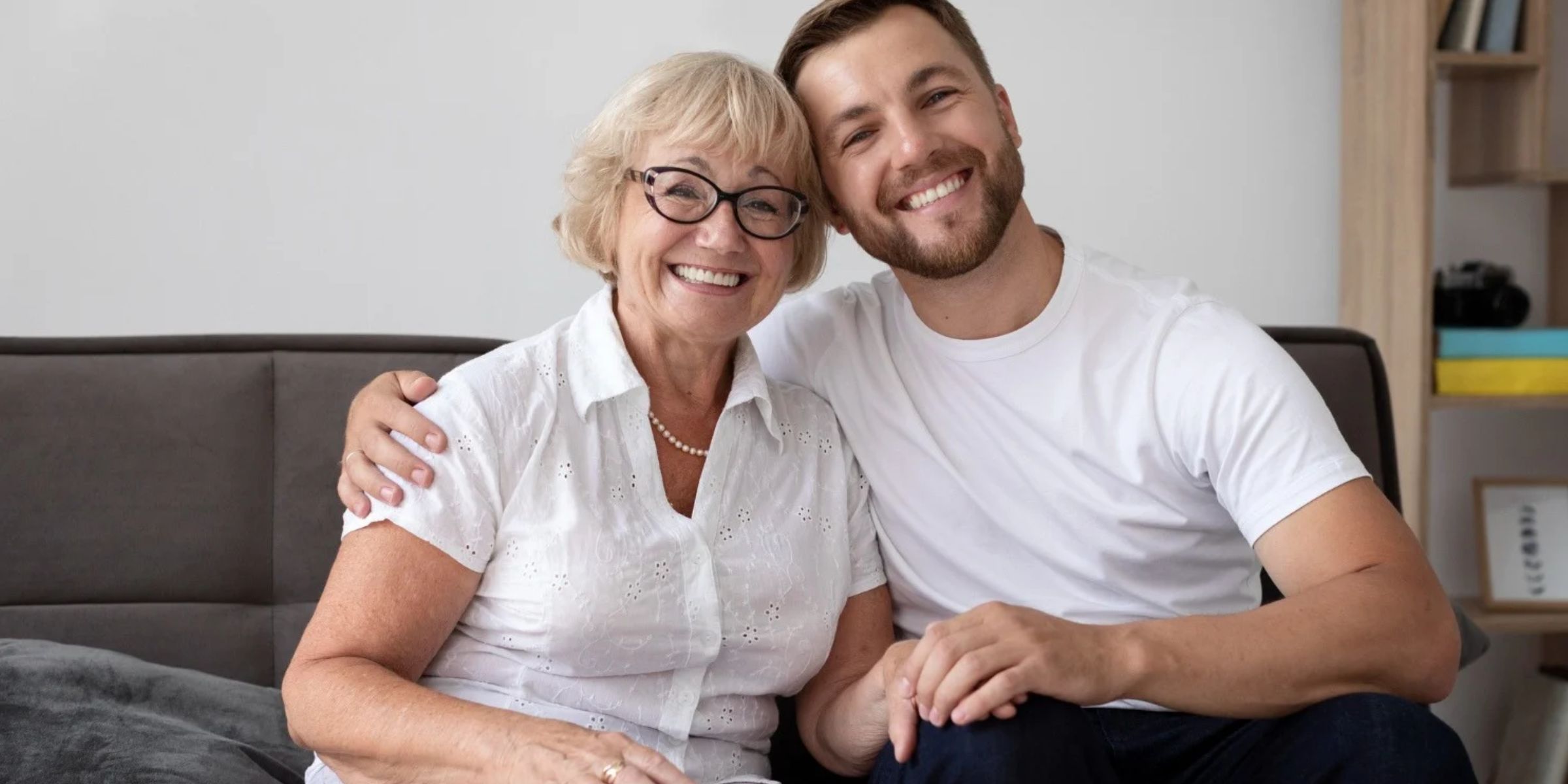 Smiling elderly mother sitting on a couch with her adult son, embracing each other | Source: Magnific