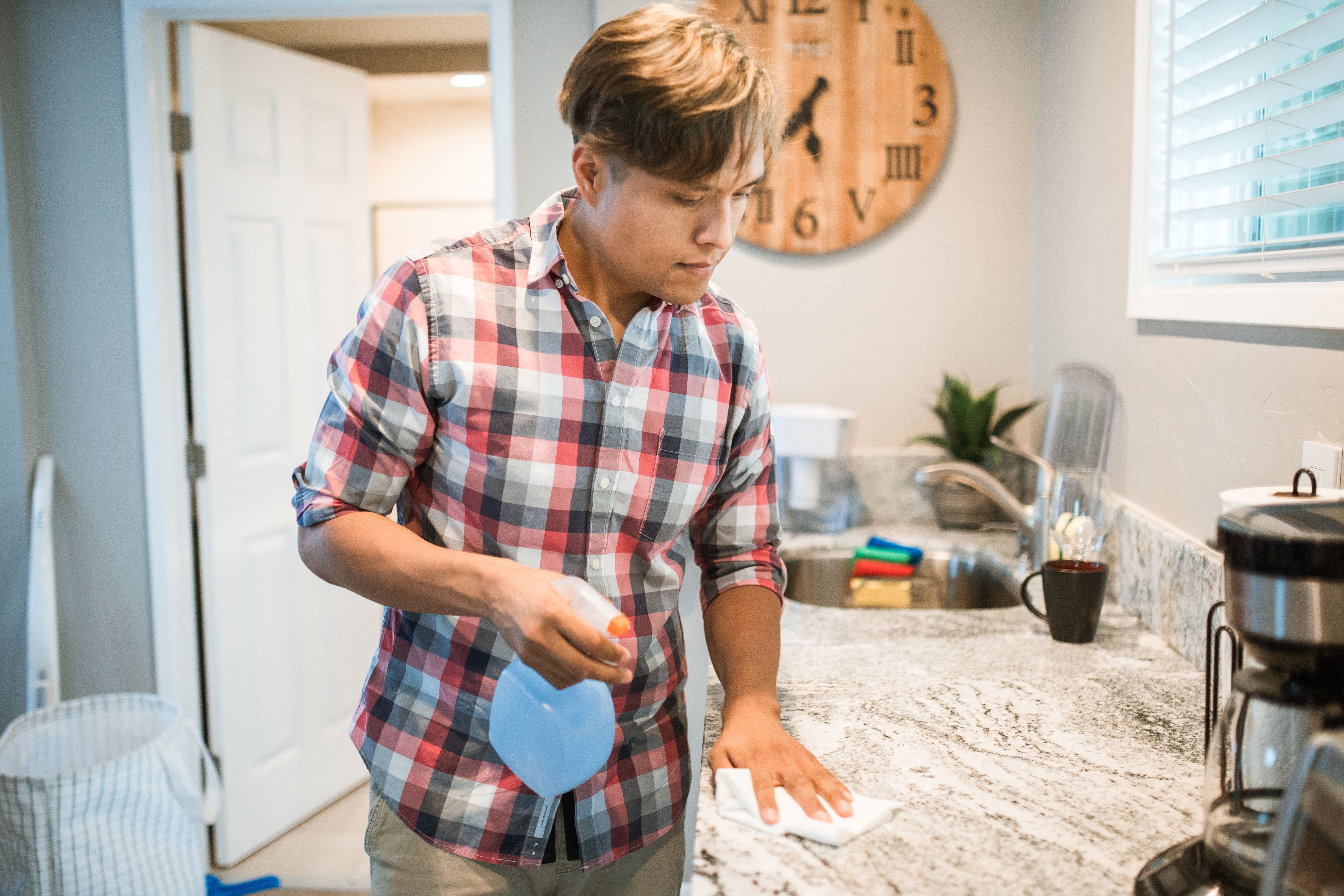 An Asian man wiping down a kitchen counter with a cleaning product in a modern kitchen | Source: Pexels