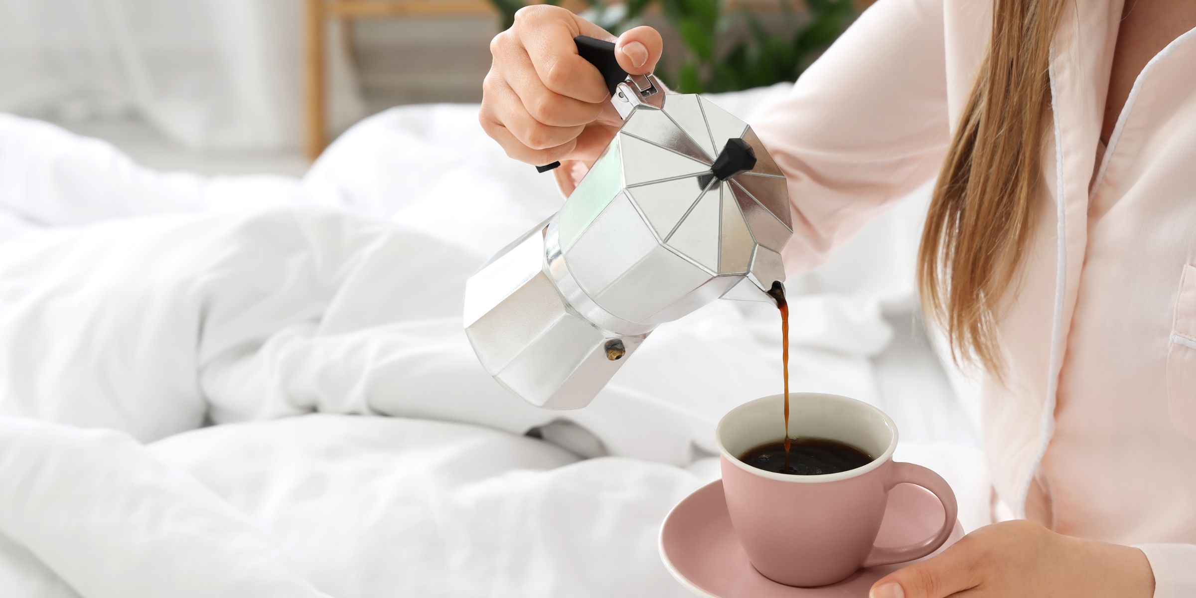 Close-up shot of a woman pouring coffee in her cup while sitting in bed | Source: Shutterstock