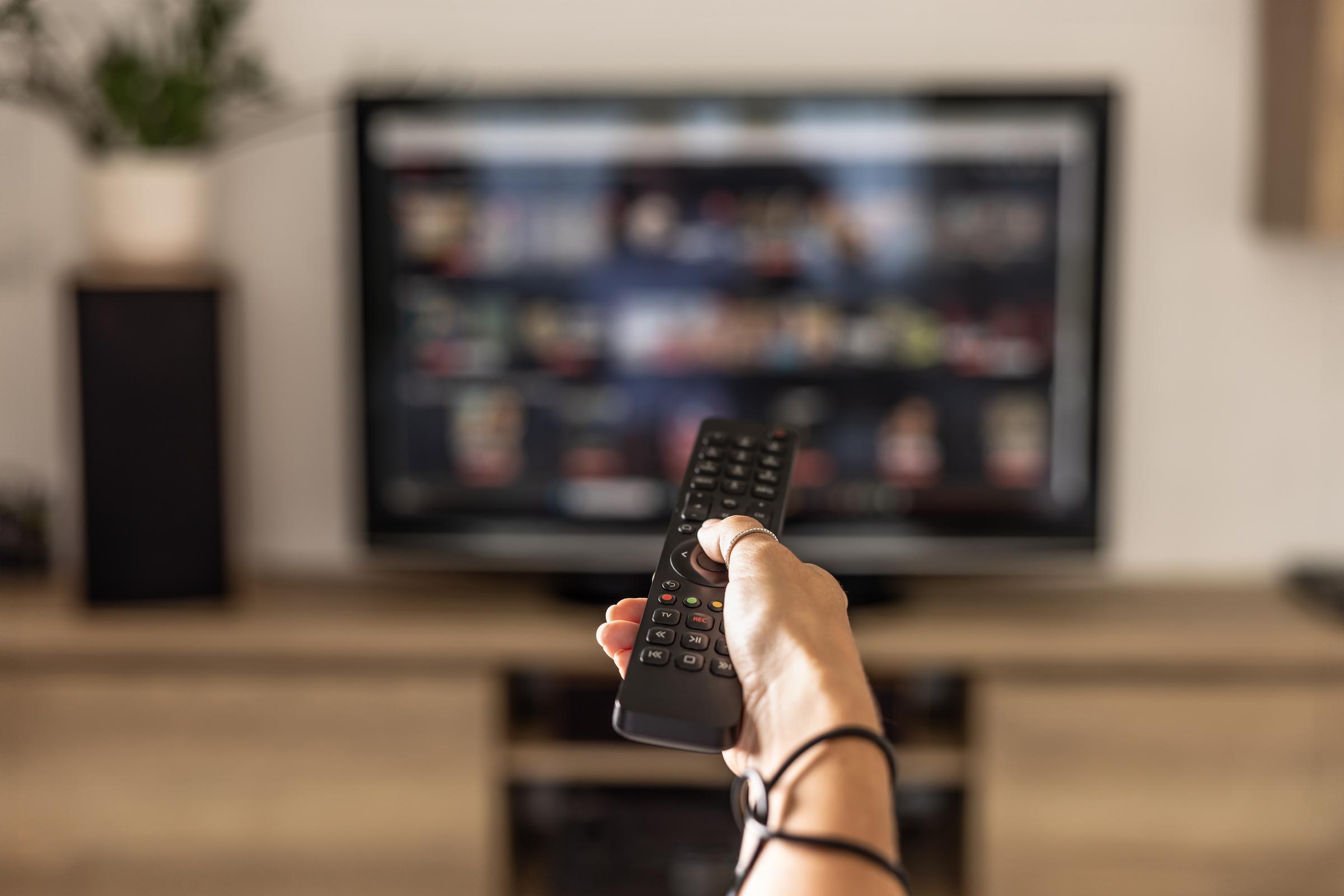A close up of a person holding a control remote with a television screen on the background | Source: Getty Images