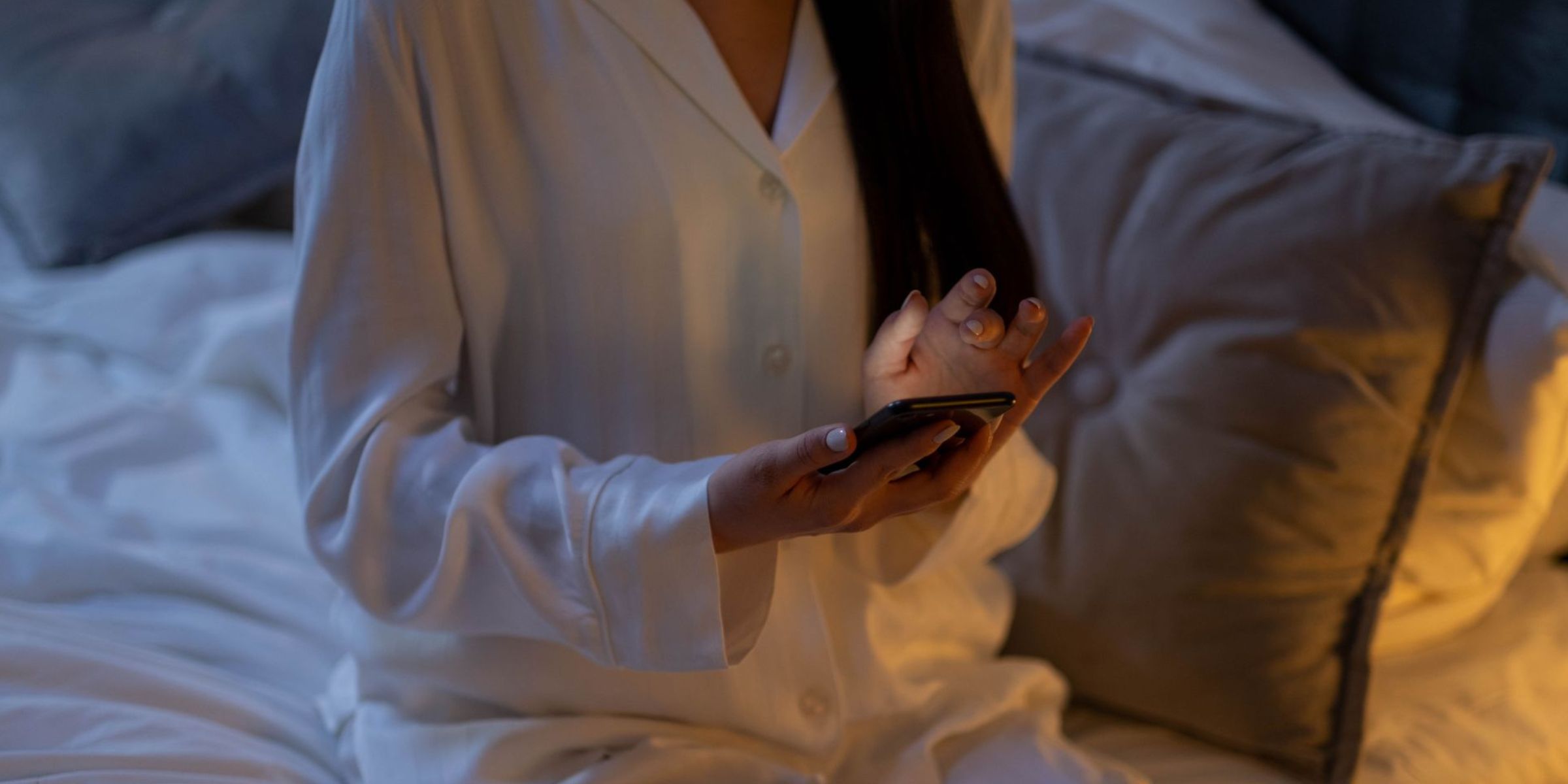 A woman in white pajamas sits on a bed and uses a smartphone at night | Source: Pexels