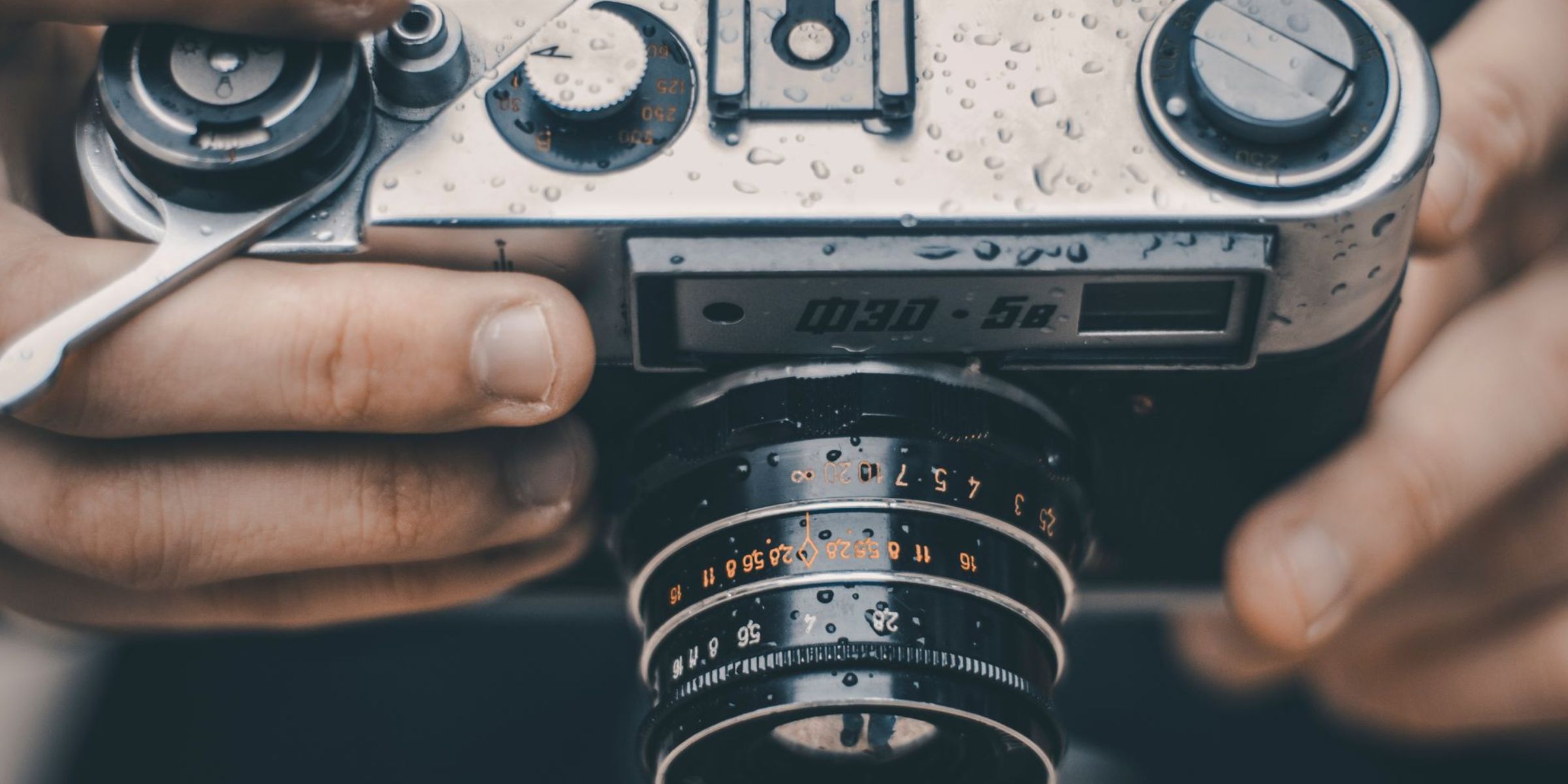 A close-up of hands holding a vintage analog camera covered in raindrops | Source: Pexels